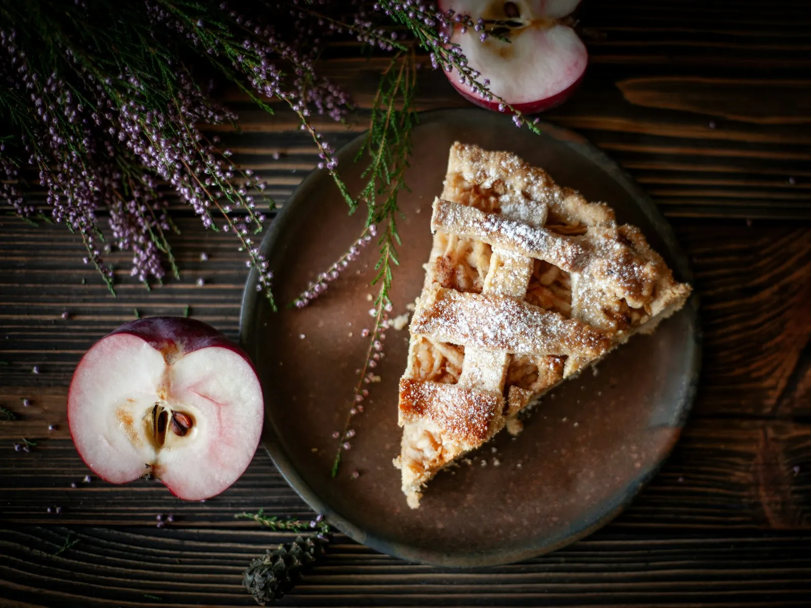 A slice of lattice-top apple pie next to a halved apple