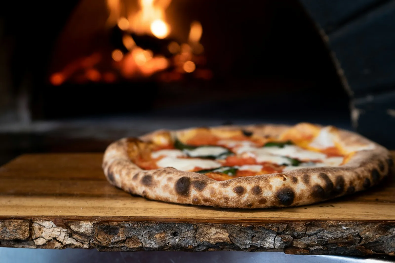 A blistered flatbread on a wooden board in front of the lit oven